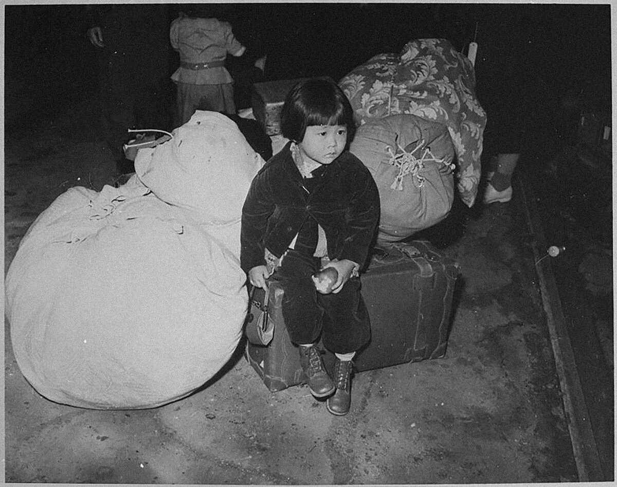 05 A young evacuee of Japanese ancestry waits with the family baggage before leaving by bus for an assembly center NARA 539959