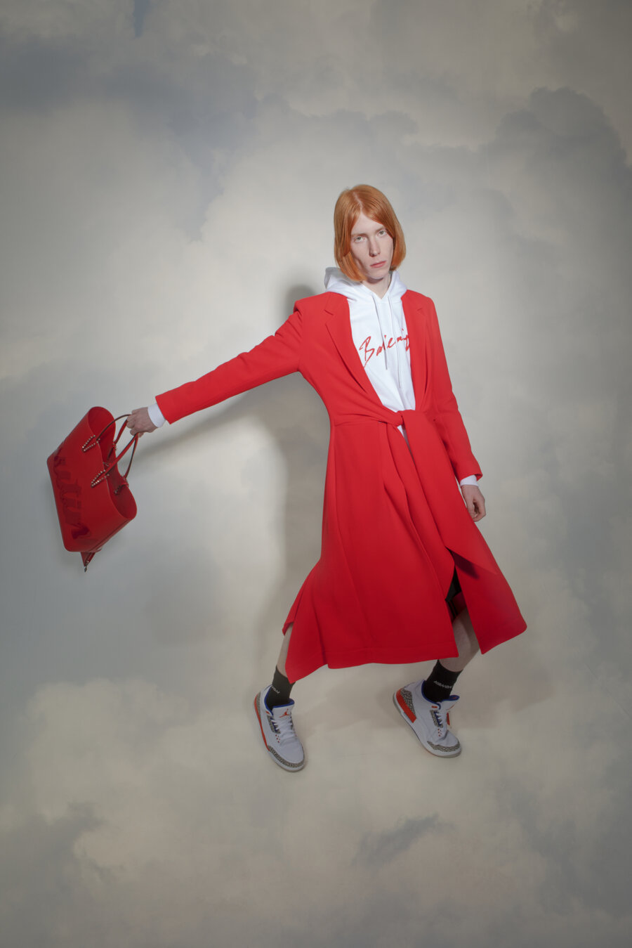 Model wearing a red coat in front of a cloud background
