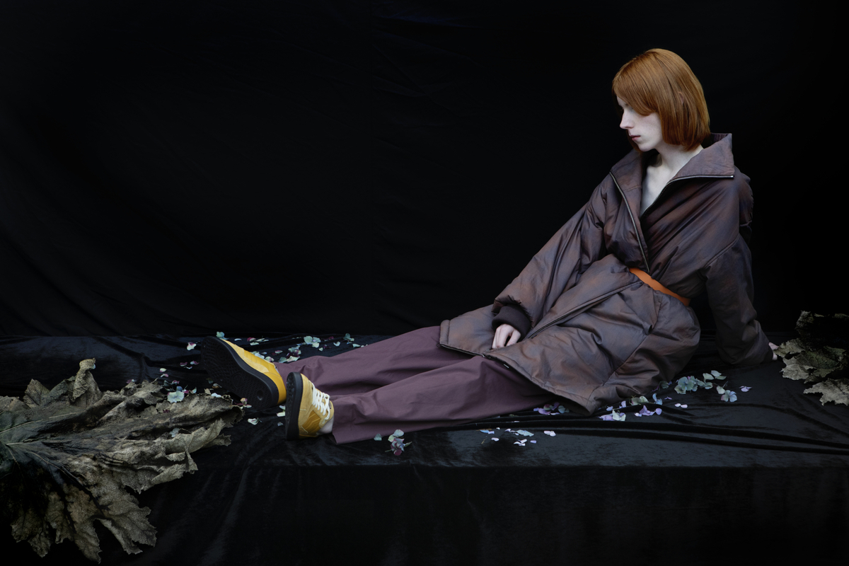 A model sitting on the ground with his feet resting on a large leaf