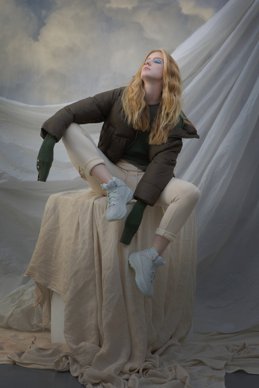 A model sitting on a cloth covered pedestal in front of a cloud background