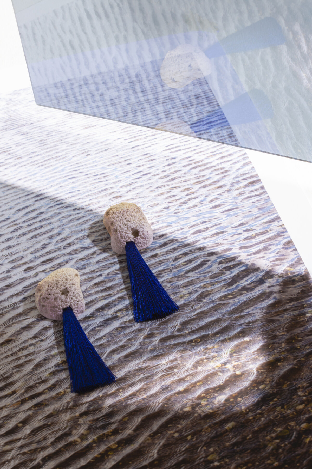 Print of beach scape with mirror on top giving reflection. A pair of Kate Trouw earrings sit on top