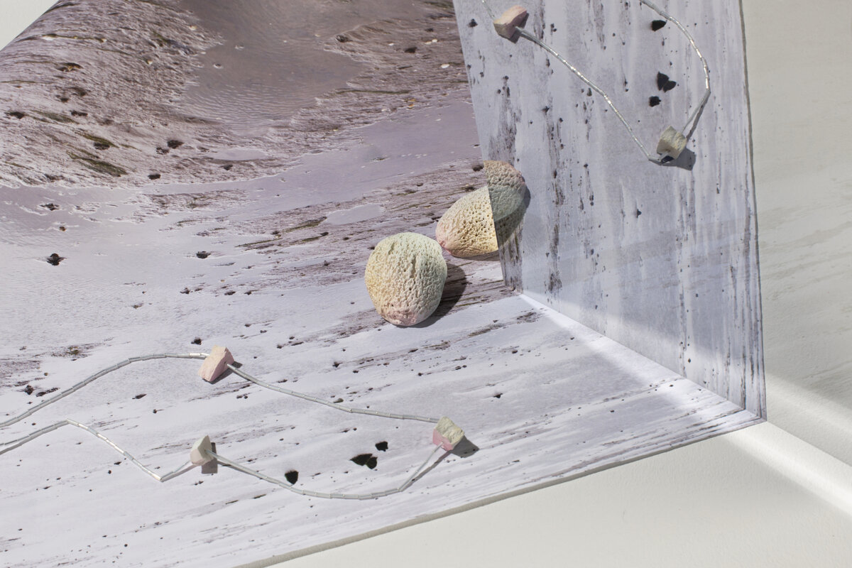 Print of beach scape with mirror on top giving a reflection. A Kate Trouw necklace and pair of earrings sit on top