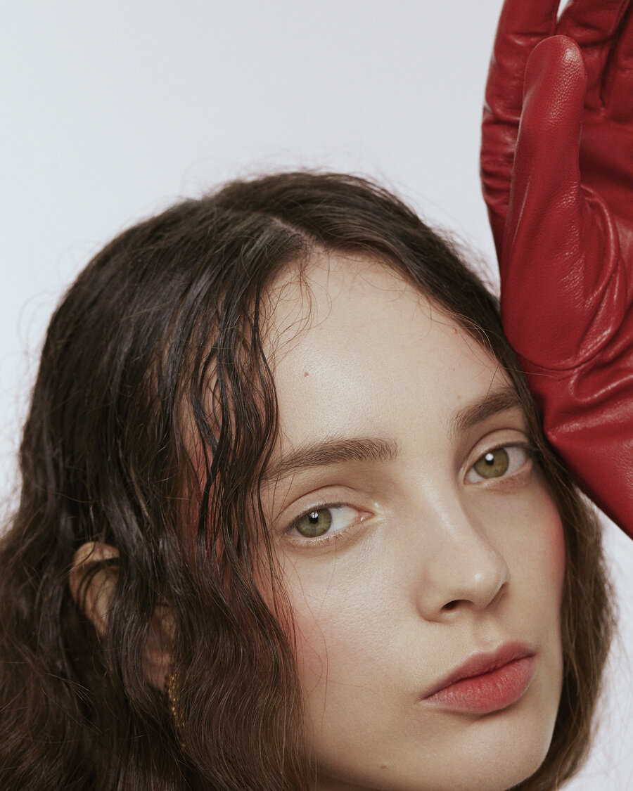 Portrait of woman with slightly wavy hair. She is wearing a red leather glove and raising her hand in the air