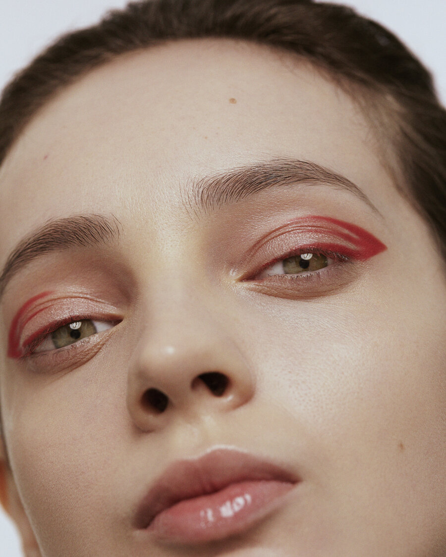 Close up of a woman's face. She is wearing pinky-red eye shadow and has her hair worn backwards