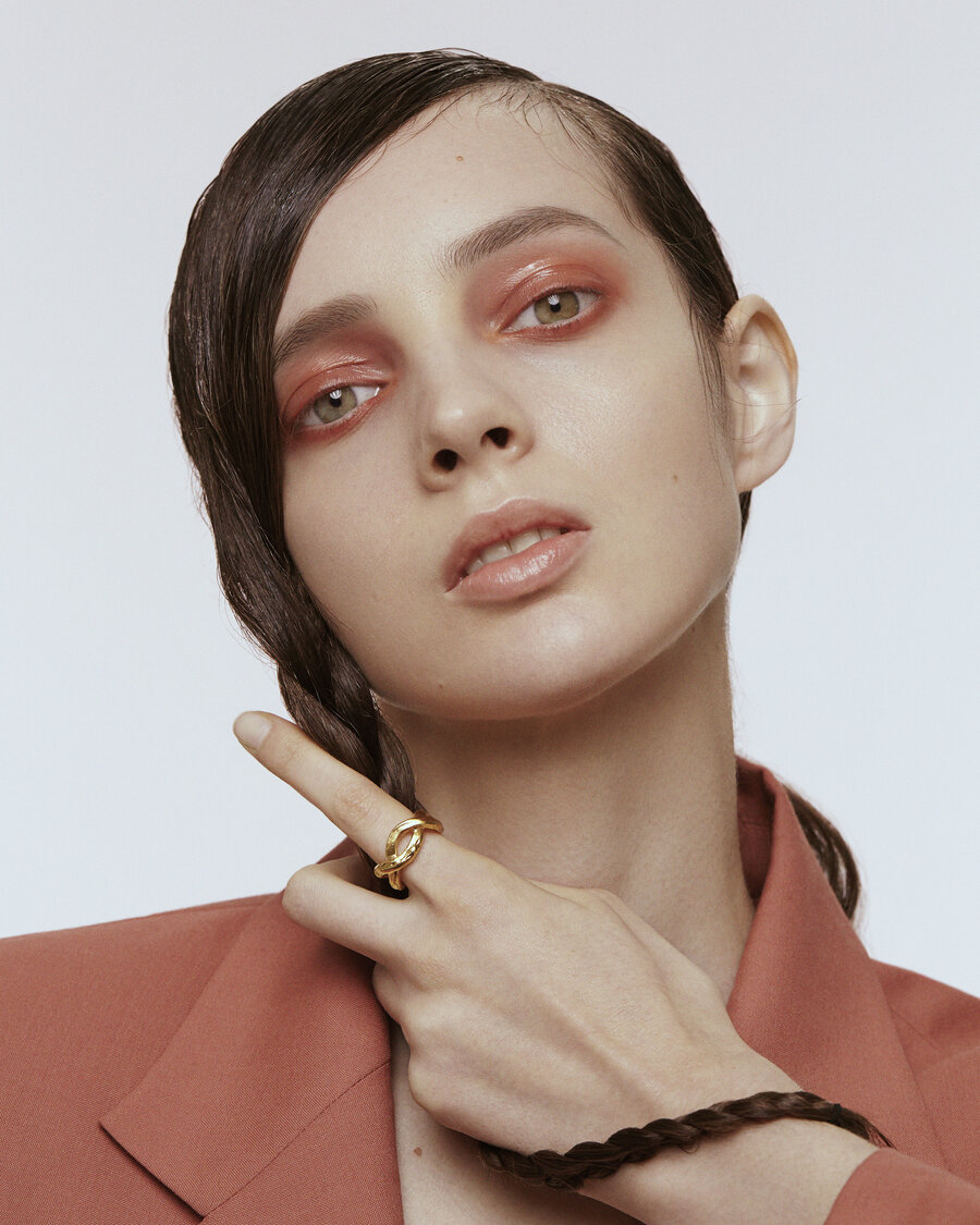 Portrait of a woman with her hair in a braid. She is wearing a gold ring on her index finger