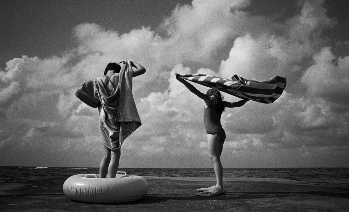 Two girls standing with towels on a beach.