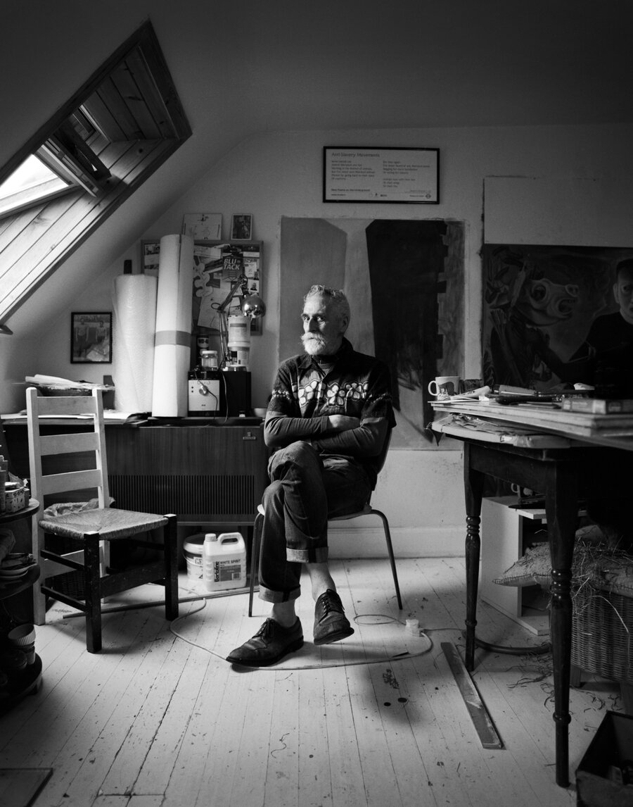 The artist John Byrne sitting with one leg crossed over the other. The room appears to be his studio.